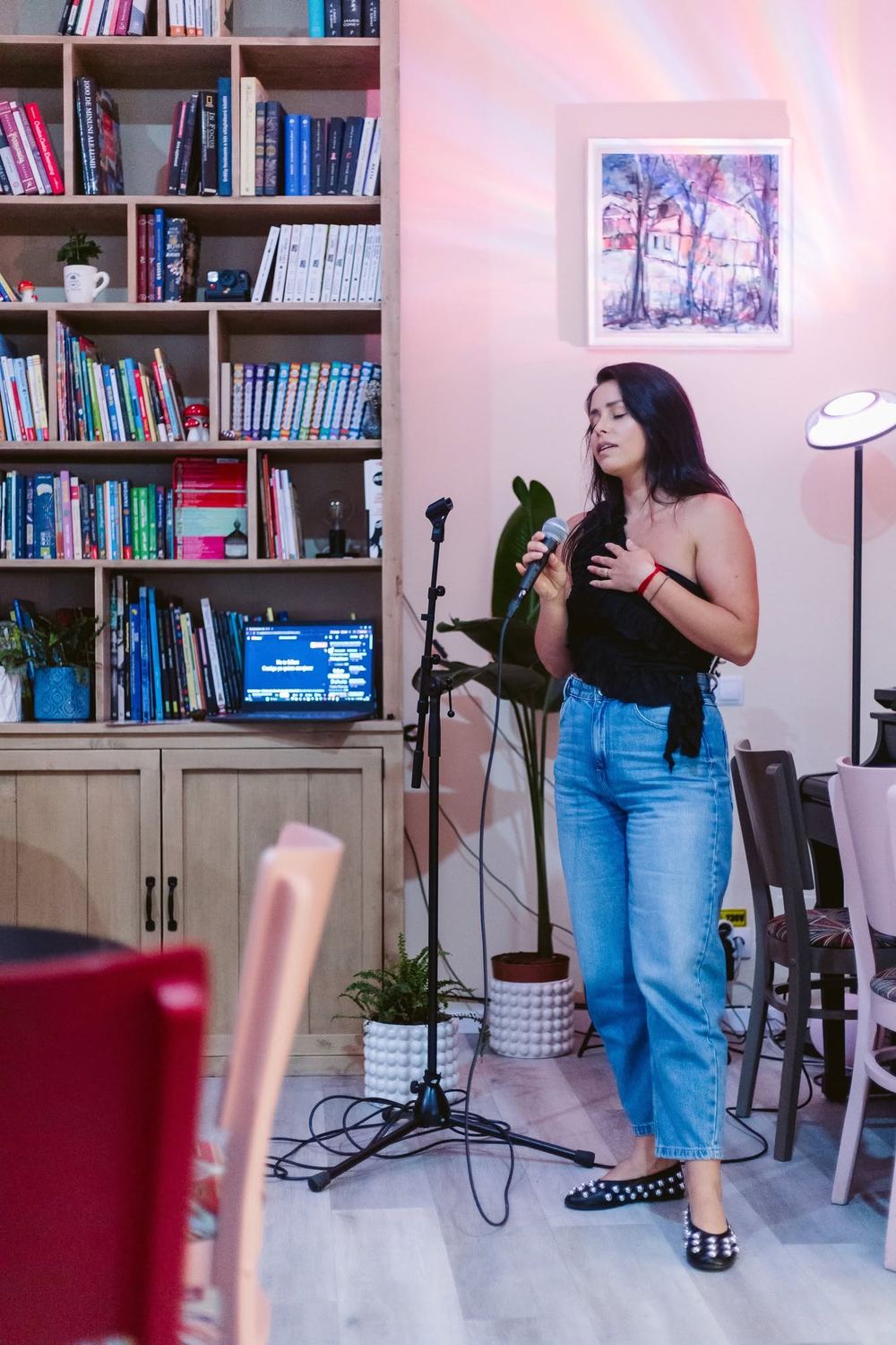 Recital de voce la Artizan HUB, solistă cu microfon în fața rafturilor de cărți